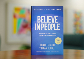 A hardcover copy of Believe in People, co-authored by Charles Koch and Brian Hooks, standing upright against a neutral gradient background.