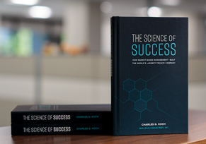 A hardcover copy of The Science of Success by Charles Koch, standing upright against a neutral gradient background.